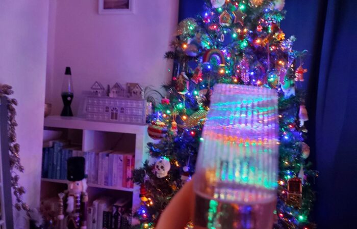 An image of a prosecco glass being held up in front of a decorated Christmas tree.