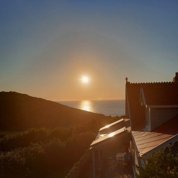 Image of a sunset over the sea, overlooking a cottage and forest