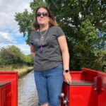 Woman in jeans, t-shirt and sunglasses standing on a red barge boat.