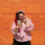 Woman wearing a pink blouse and pink glasses looking on her phone screen
